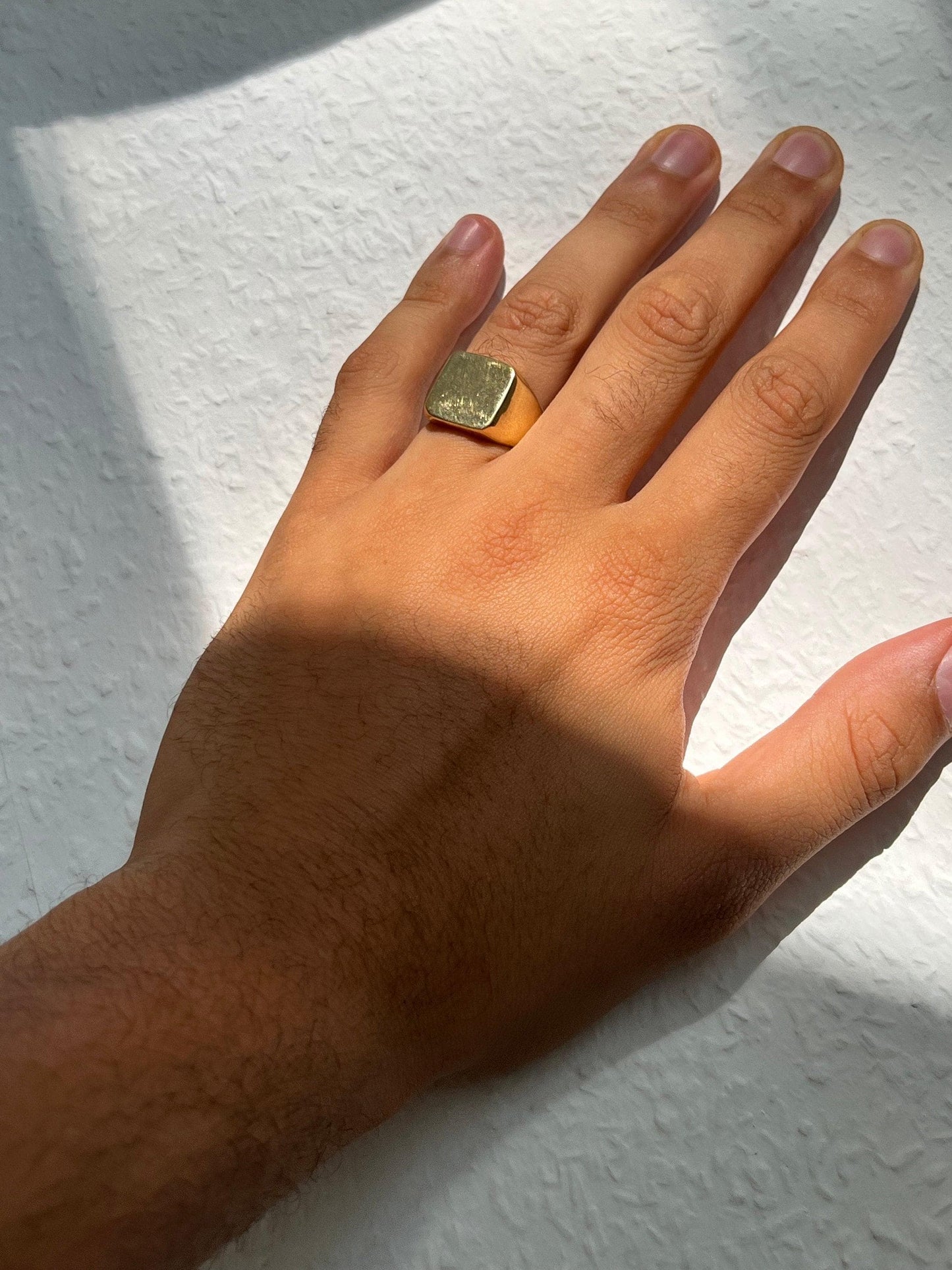 Könnte beinhalten: Ein goldener quadratischer Siegelring an einer Hand.