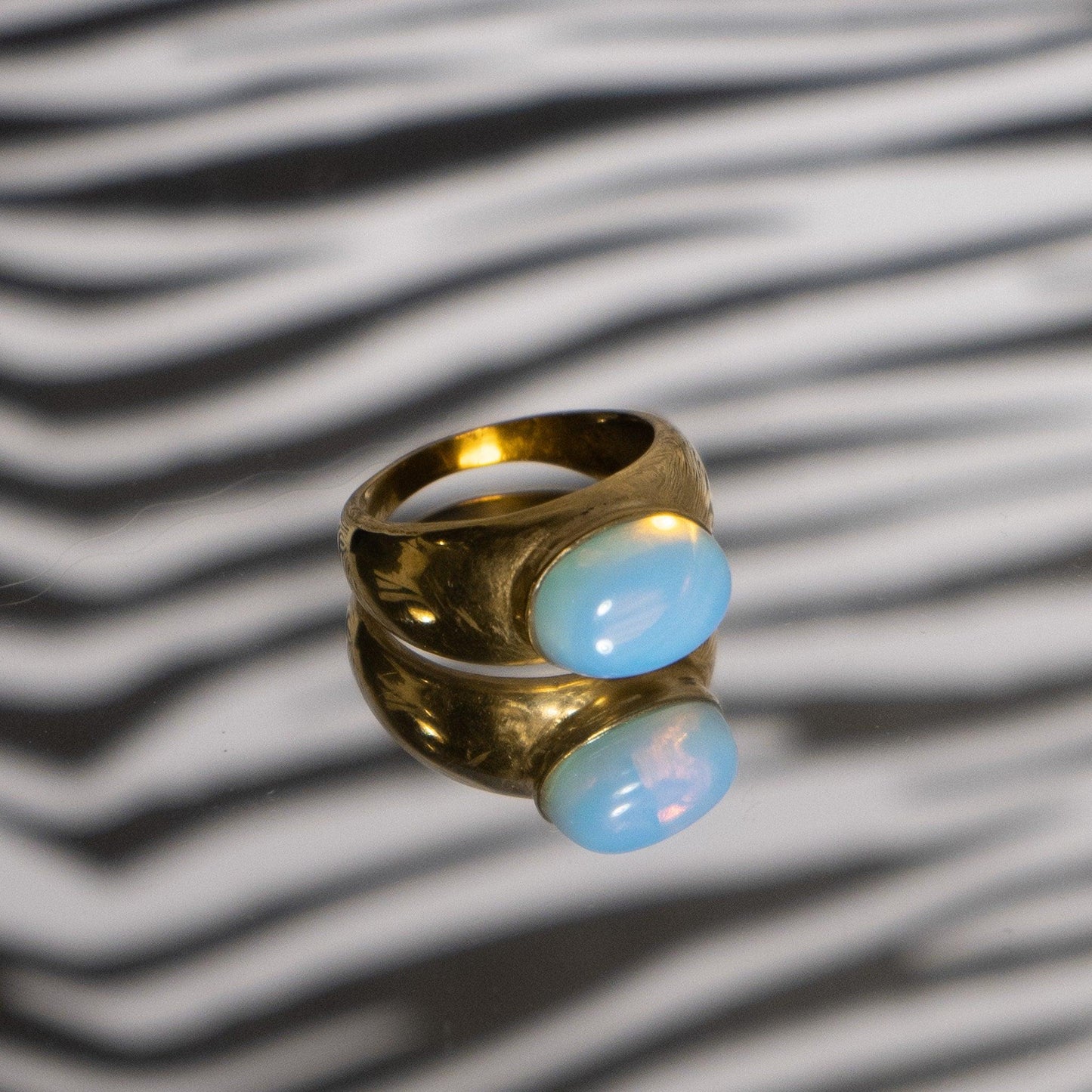 Könnte beinhalten: Ein goldener Ring mit einem hellblauen ovalen Edelstein. Der Ring liegt auf einer Oberfläche mit Zebra-Muster.